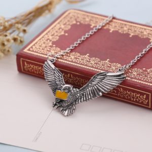 Collier hibou avec lettre de Poudlard jaune Harry Potter posé sur un livre